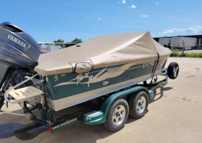 Profile view of a boat featuring green accent stripes on a trailer, wrapped perfectly in a custom tan marine canvas ratchet cover.