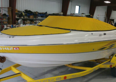 Front-angle view of a white and yellow boat on a trailer, fitted with custom yellow two-piece snap-on covers over the bow and cockpit.